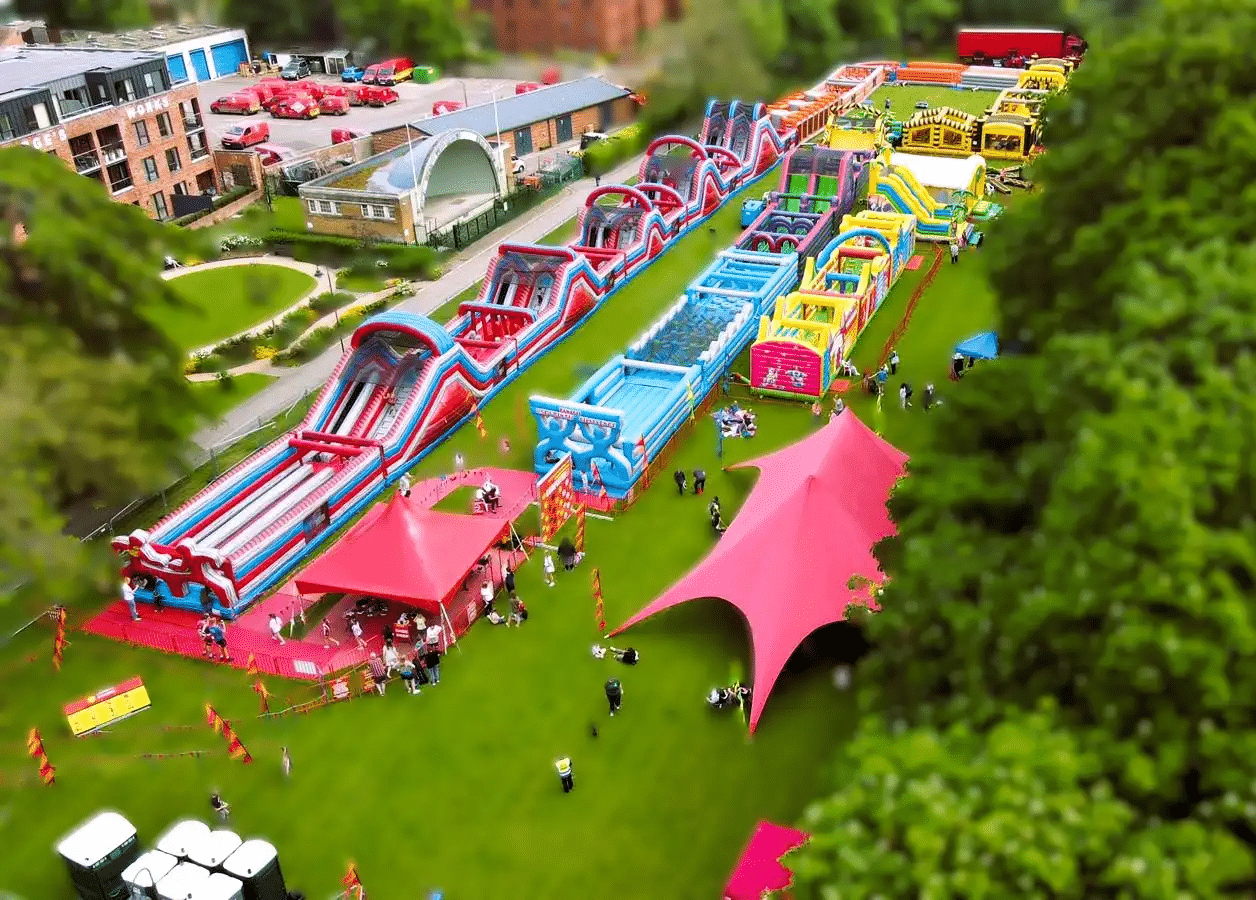 A large outdoor inflatable obstacle course with colorful tents and people on a grassy field.