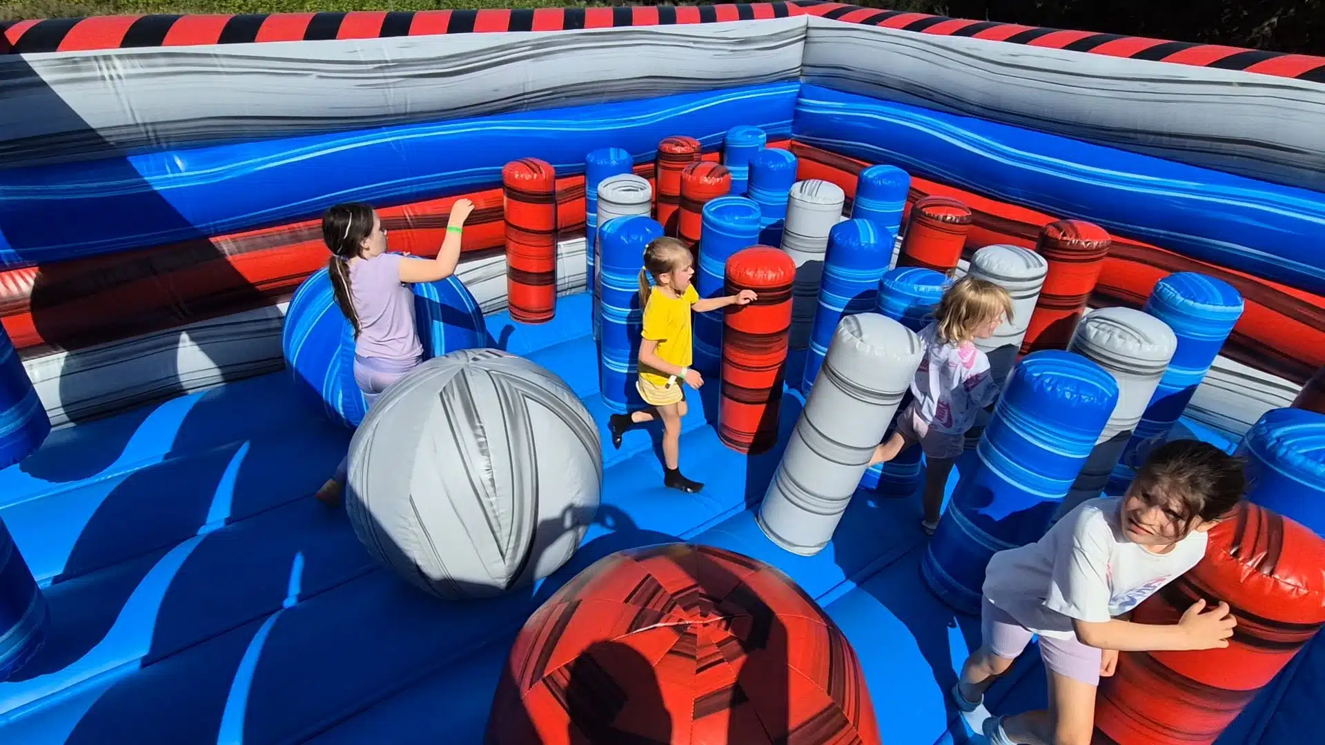 Children play inside a colorful inflatable maze with blue, red, and gray pillars.