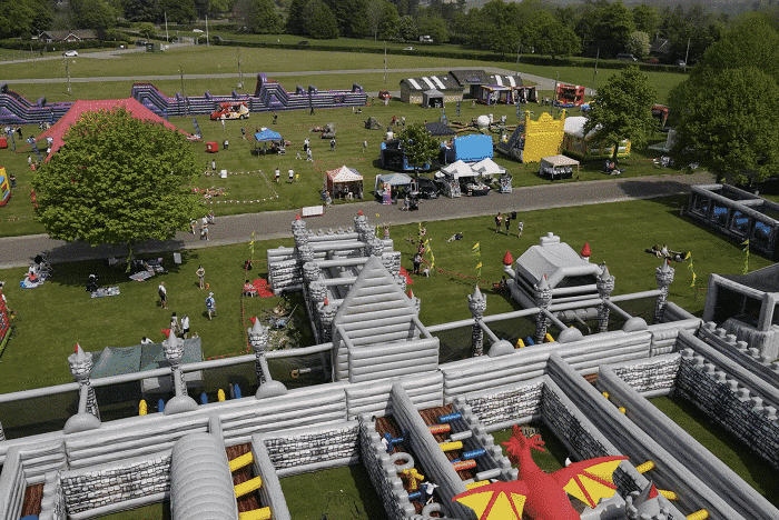 Aerial view of a park with an inflatable castle maze, people, and festival booths.