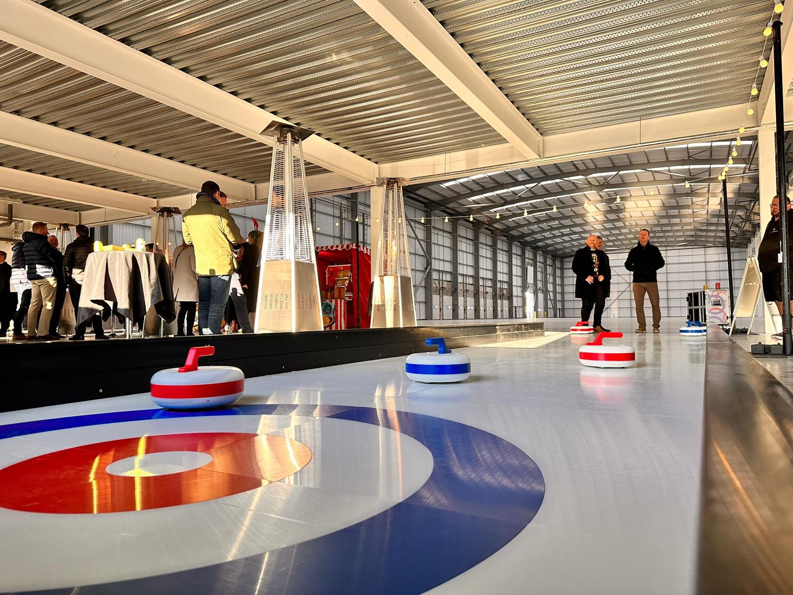 People play curling indoors with several curling stones on the ice.