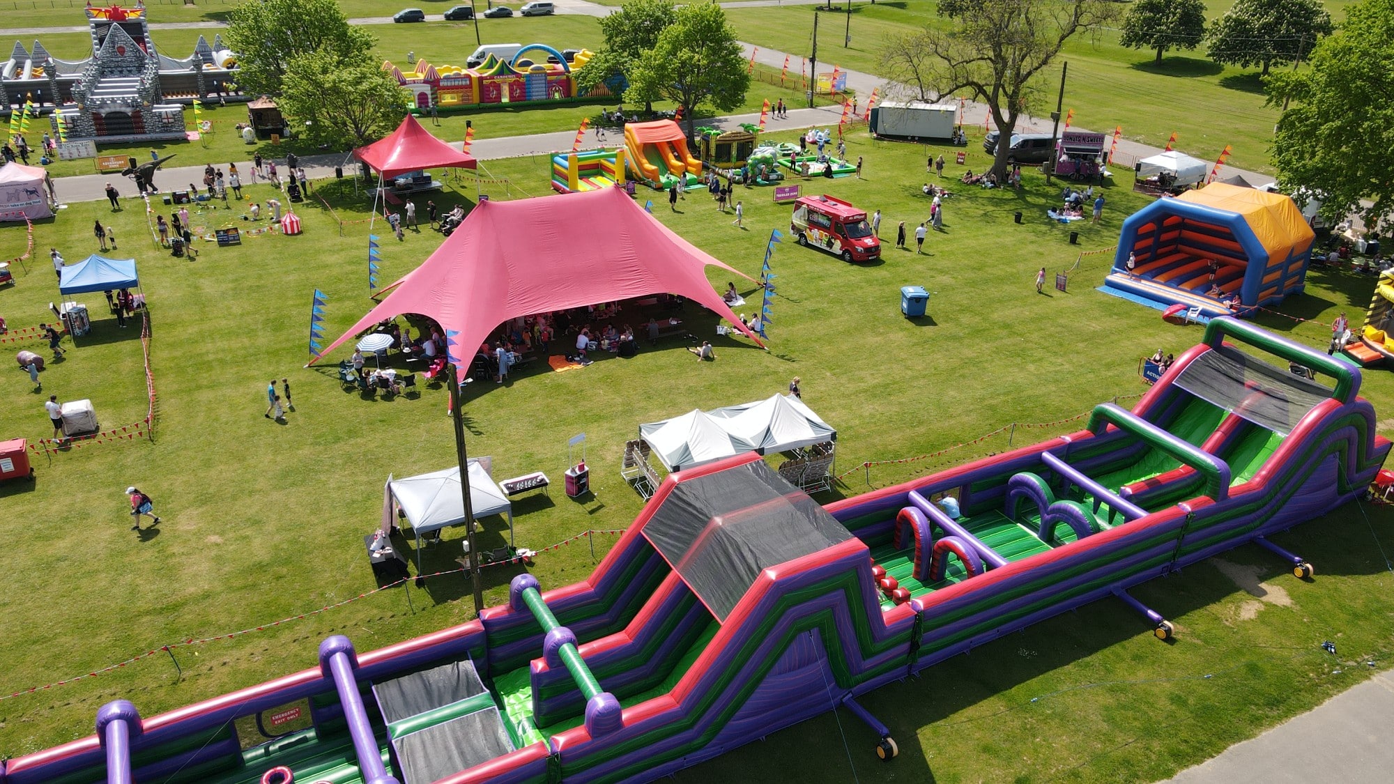 A park festival with tents, bounce houses, food trucks, and people enjoying outdoor activities.