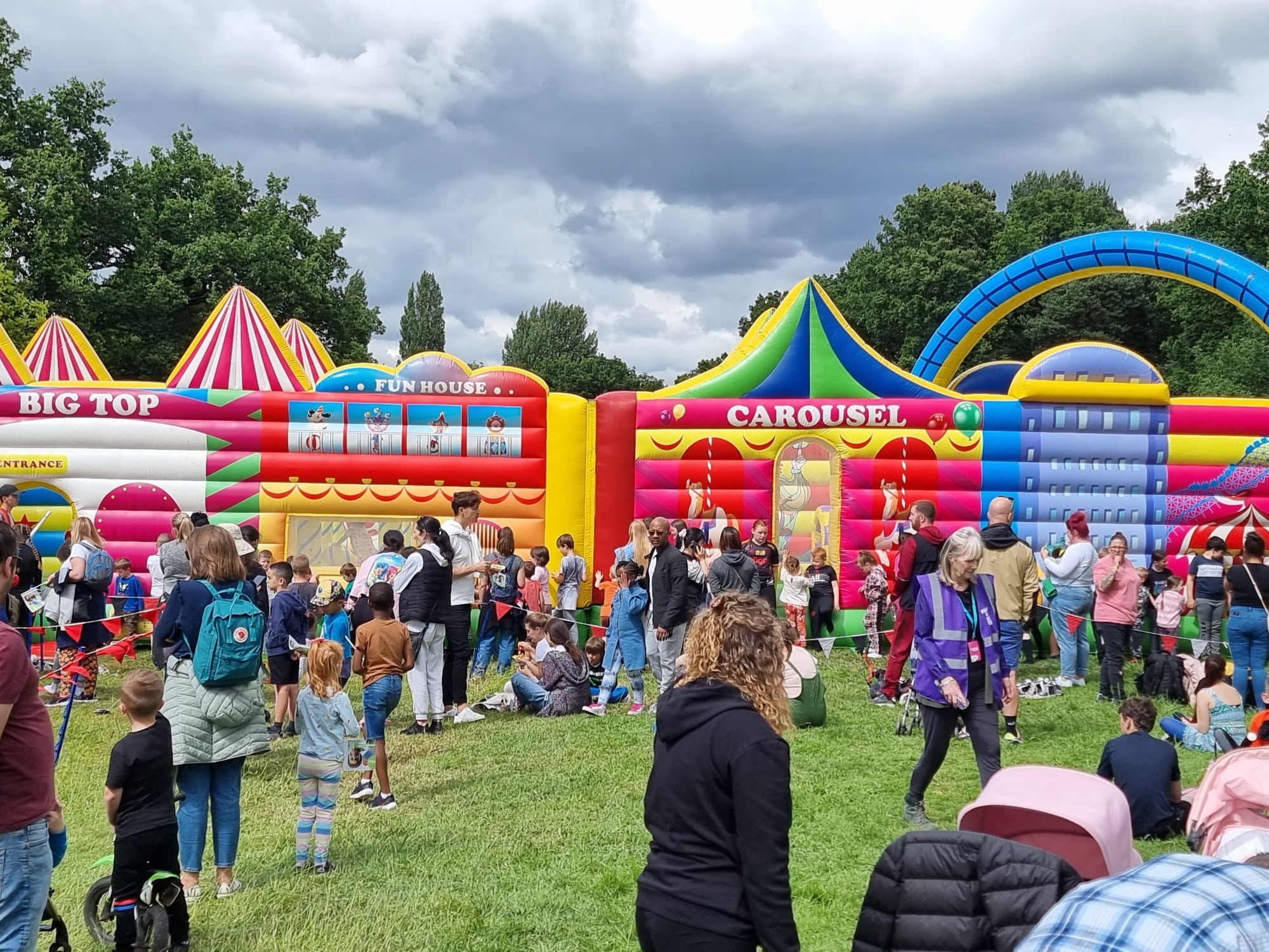 Crowd of people and children at a fun fair with colorful inflatable attractions in a park.