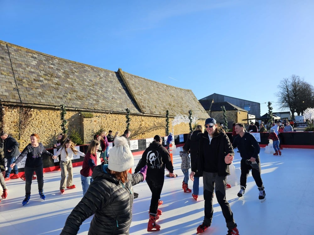 People ice skating outdoors on a sunny day near stone buildings.