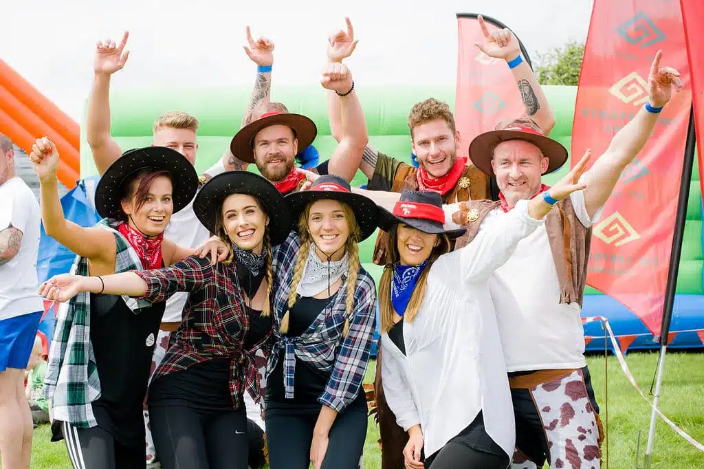 Group of people dressed in cowboy hats and bandanas smiling outdoors at an event.