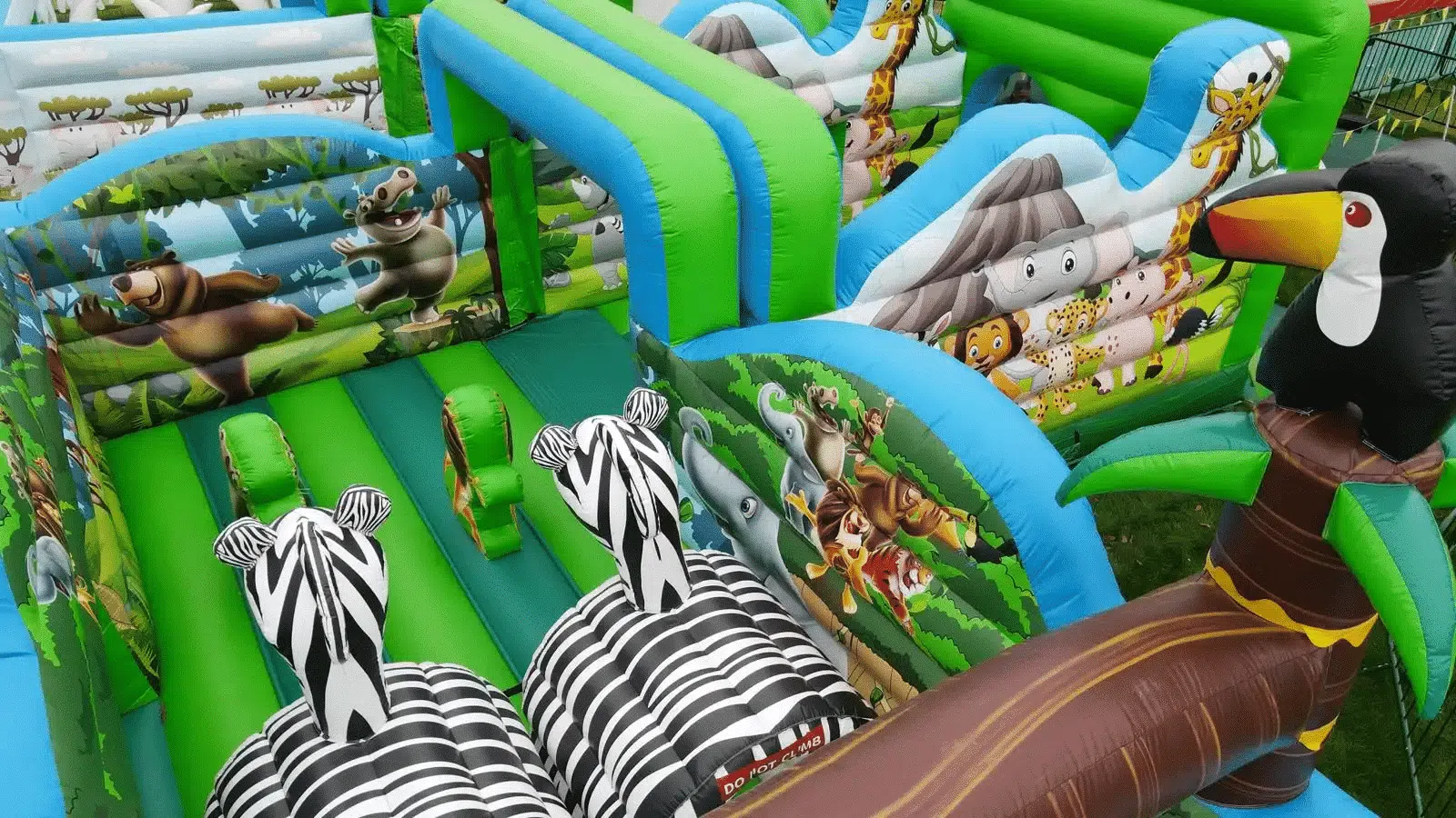 Colorful inflatable safari-themed obstacle course with zebra, toucan, and cartoon animal designs.