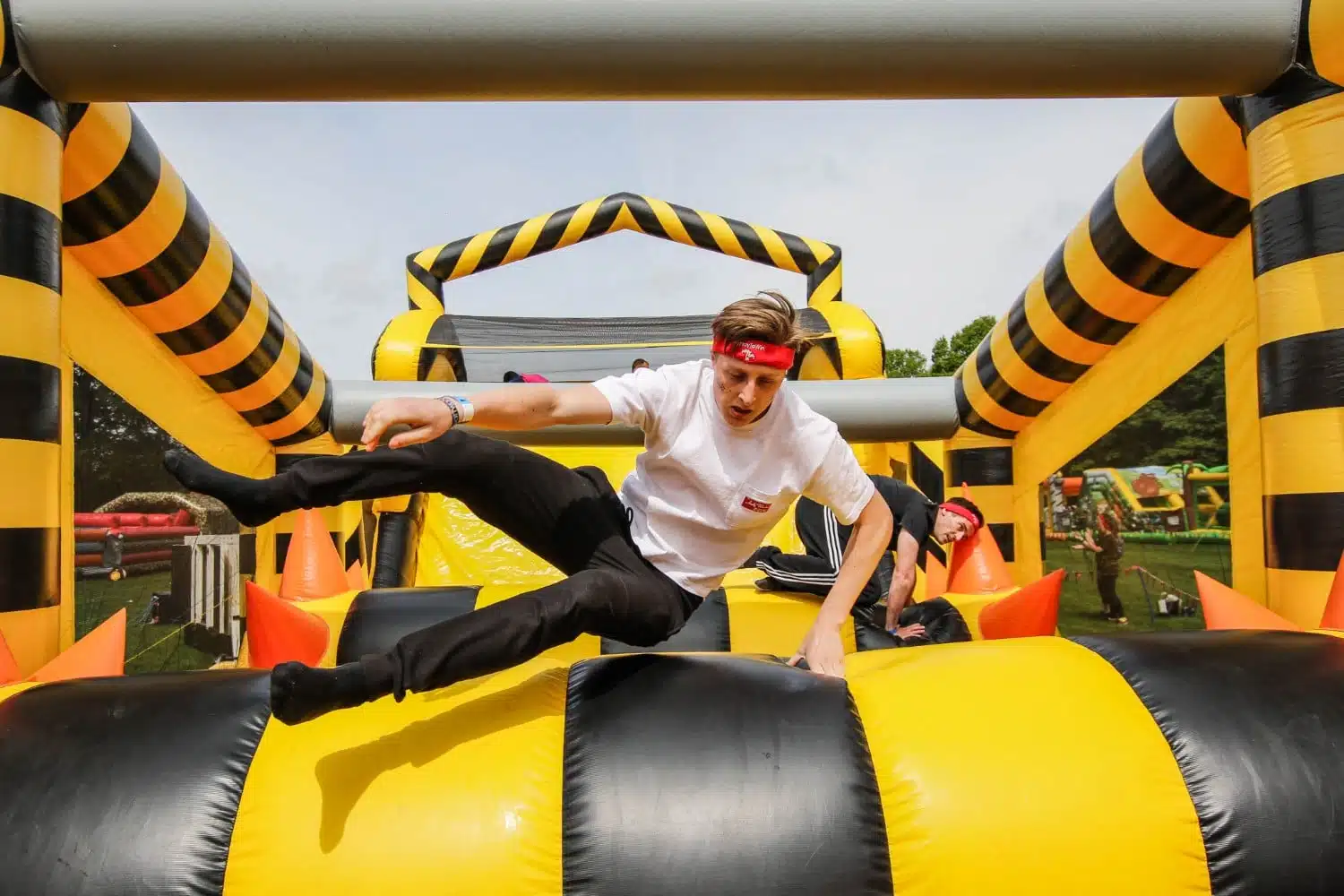 A person jumps over an obstacle in a yellow and black inflatable course outdoors.
