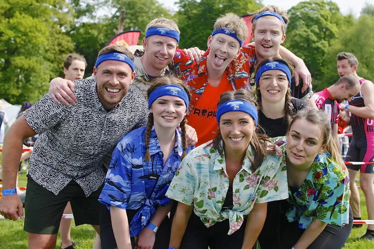 Group of people in colorful shirts and blue headbands smiling outdoors at an event.