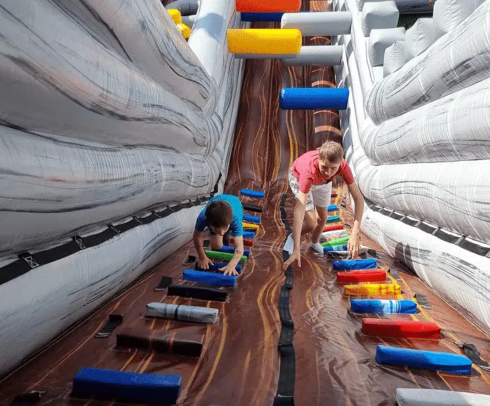 Two people climbing a colorful inflatable ladder inside a play structure.