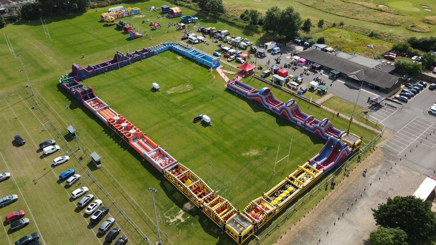 LabyrinthTour Aerial view of a large outdoor inflatable obstacle course surrounded by fields, cars, and tents.