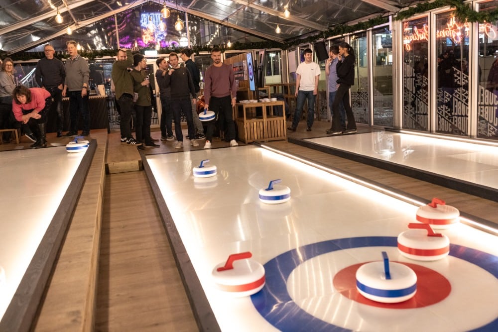 People play indoor curling on illuminated lanes at a pop-up venue in London.