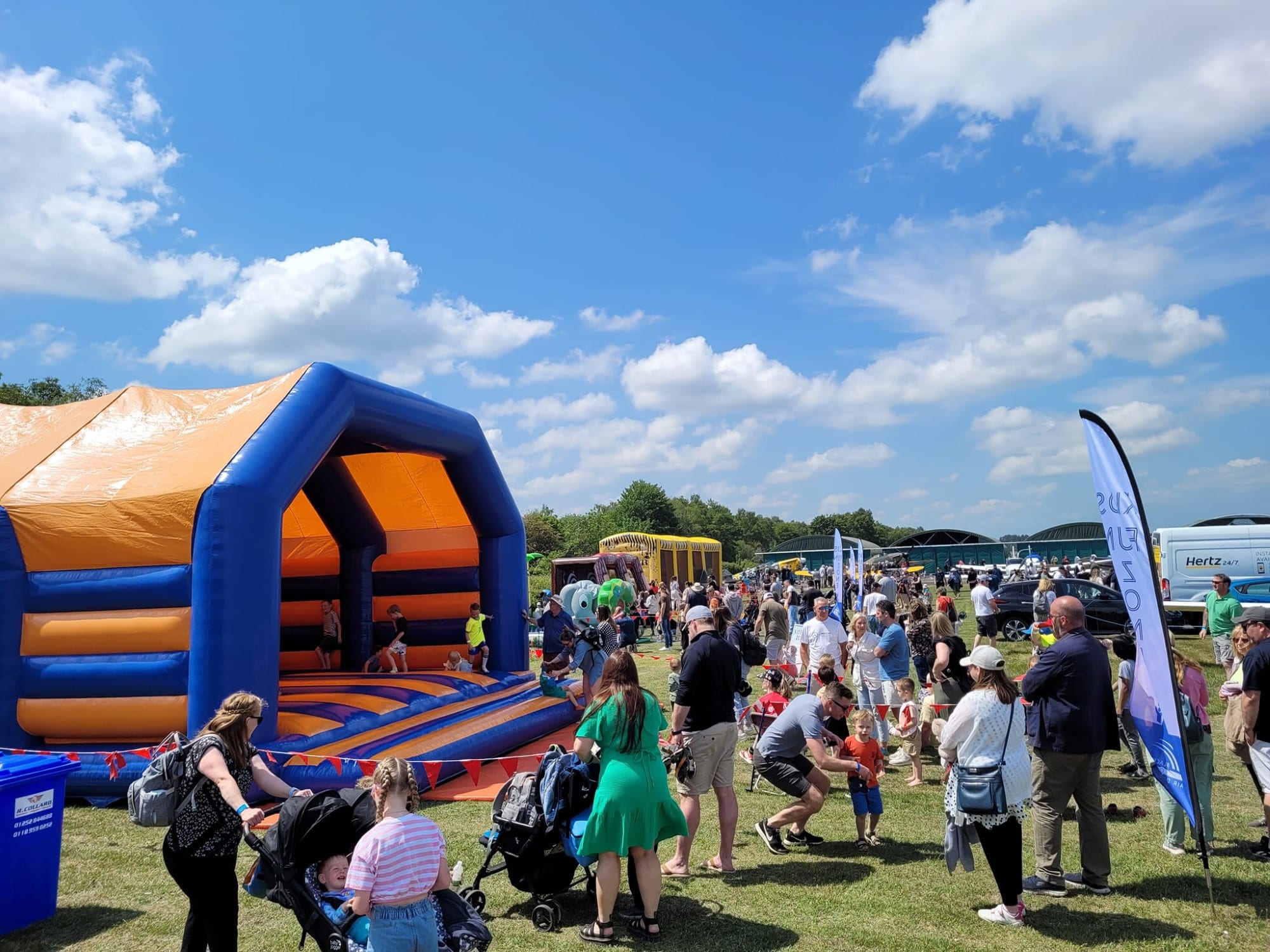 Crowd of people at an outdoor festival, with a large inflatable bounce house under a sunny sky.