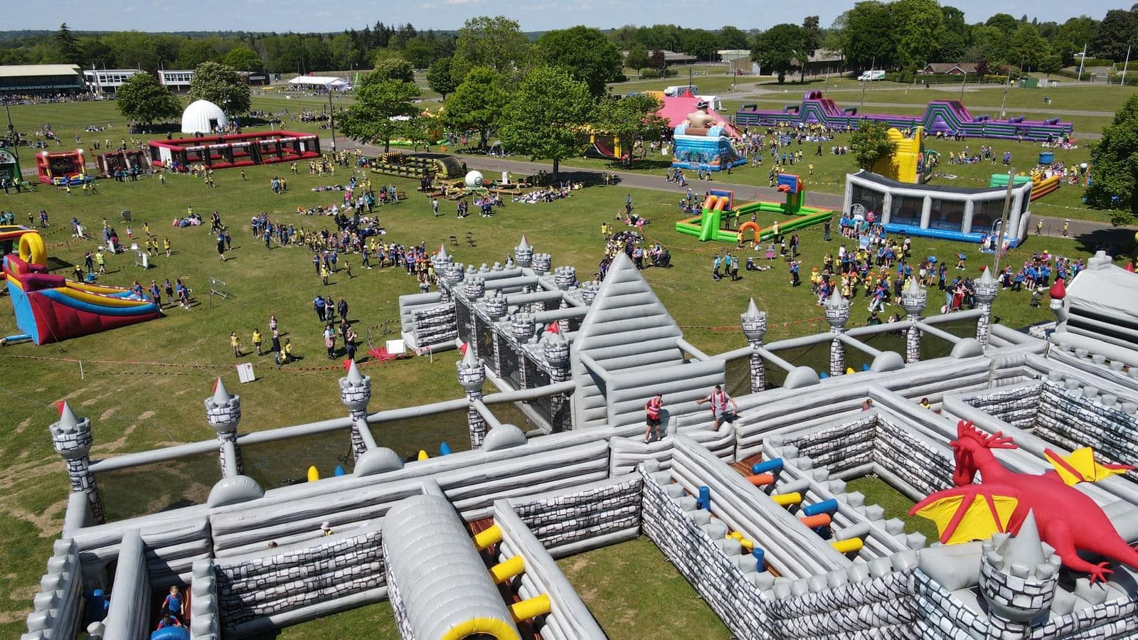 Aerial view of a large outdoor event with inflatable castles, slides, and many people on a grassy field.
