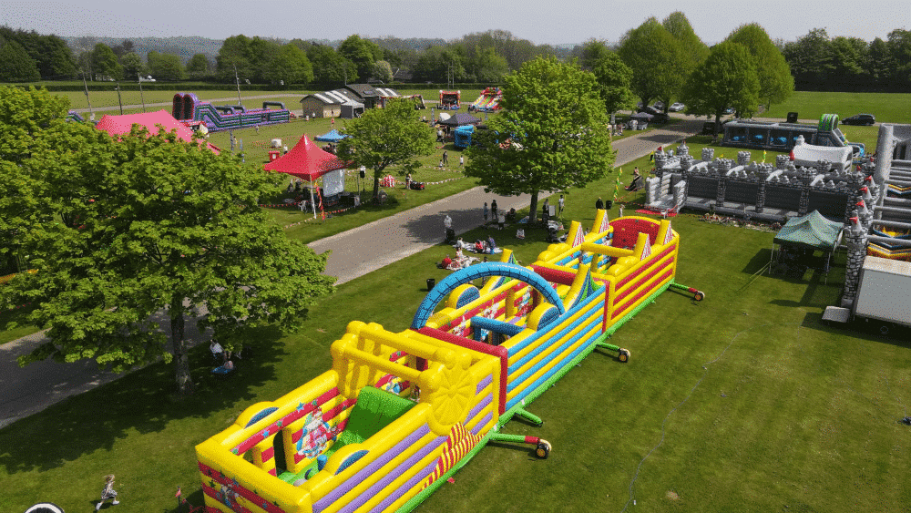 Colorful inflatable obstacle courses and tents set up in a park for a family festival event.