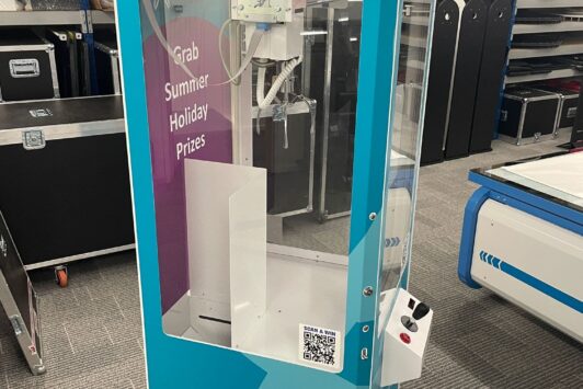 A blue prize claw machine labeled "THE CLAAAW" standing in an office or warehouse.