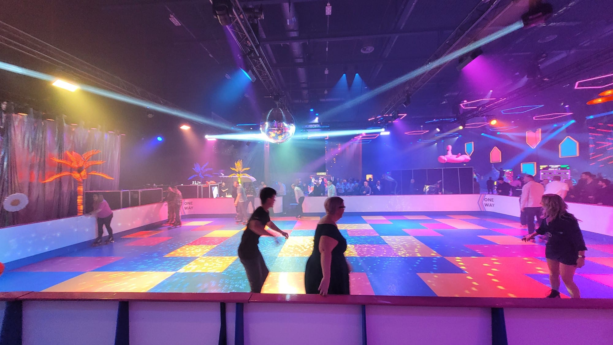 People roller skating on a colorful disco rink under bright lights and a shiny disco ball.