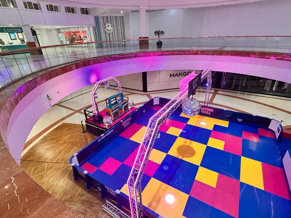 Colorful roller rink with disco ball inside a shopping mall, viewed from above.