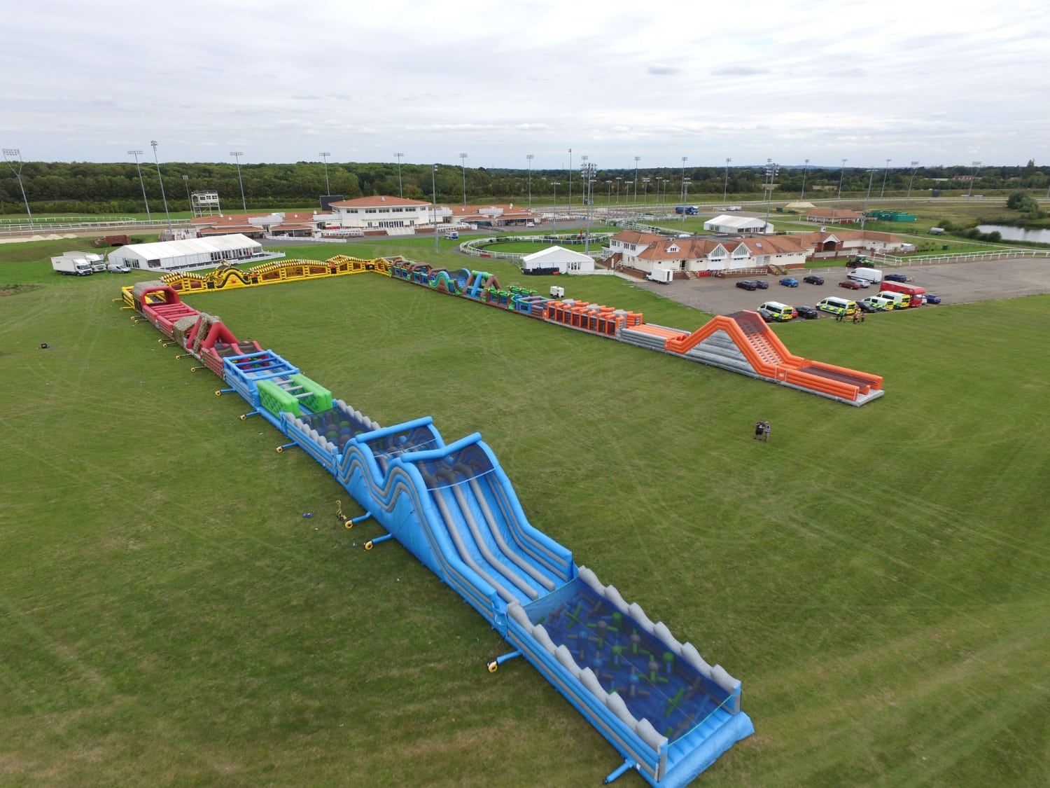 A large inflatable obstacle course is set up on a grassy field near buildings and parked cars.