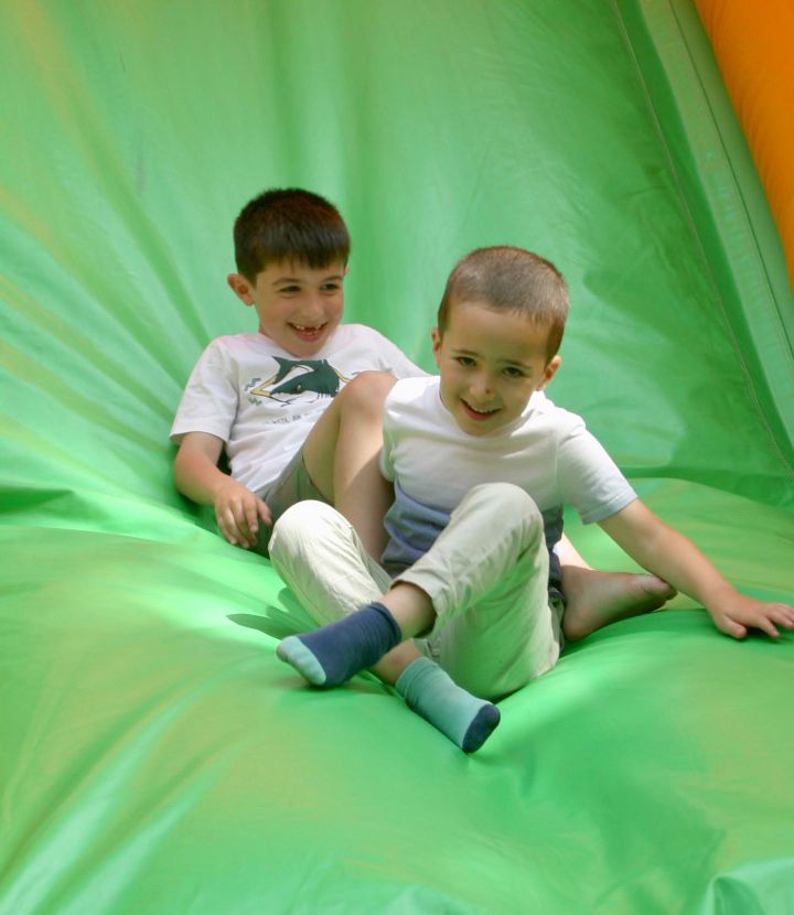 Smiling Kids Two smiling boys slide down a green inflatable slide.
