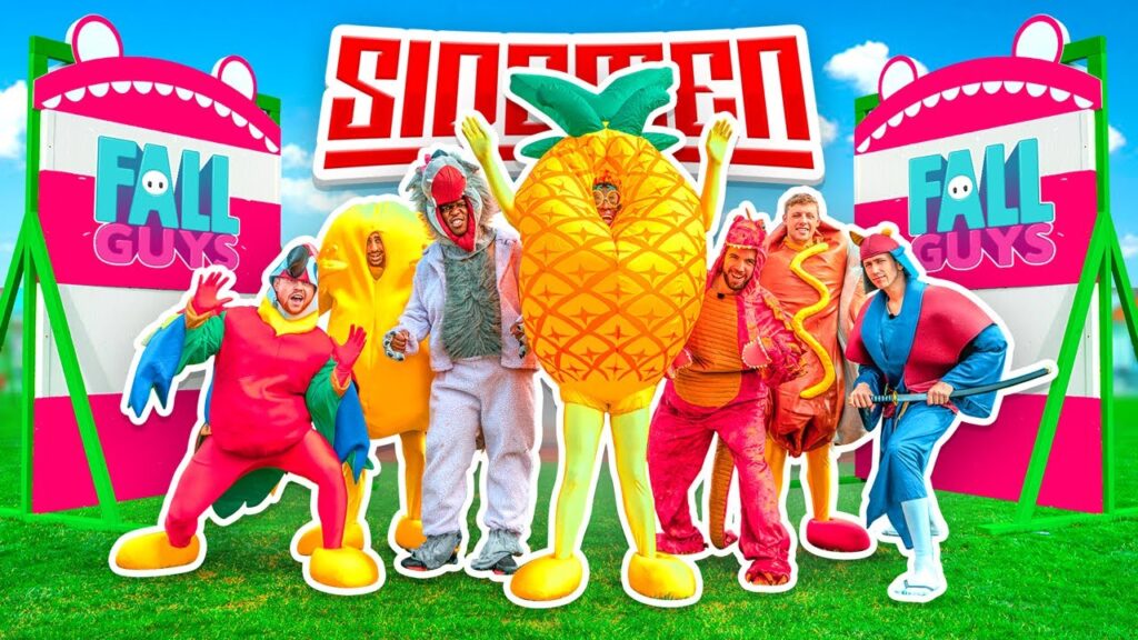 Seven people in colorful costumes pose outdoors by "Fall Guys" and "Sidemen" signs.