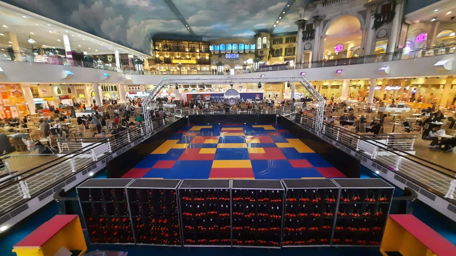 Indoor roller rink with colorful floor, surrounded by dining tables and a large mall interior.