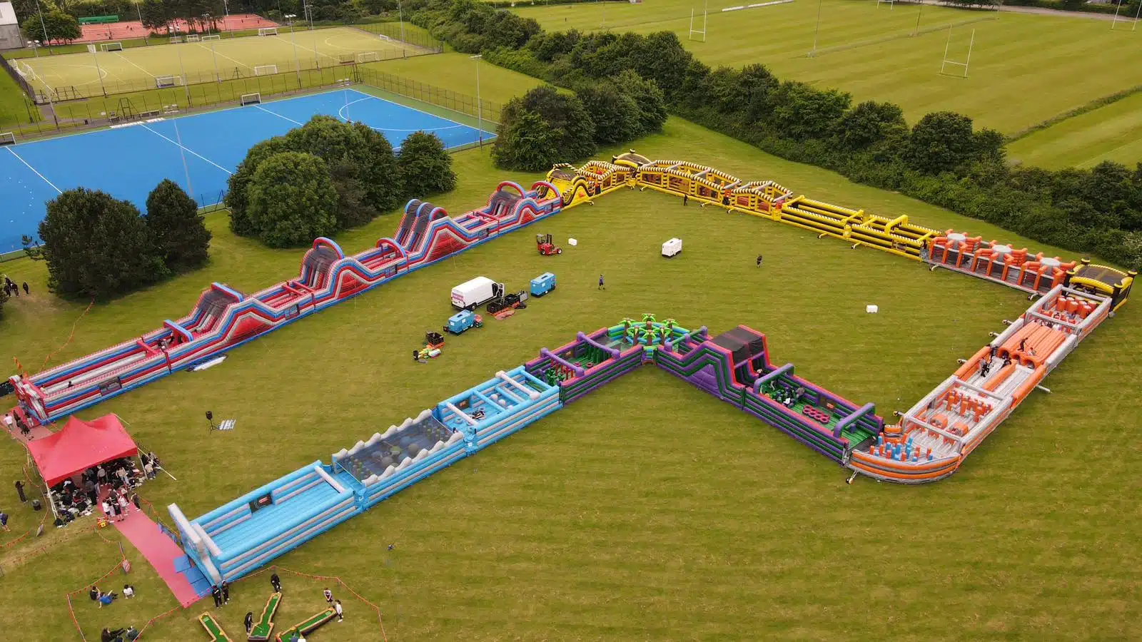 Large inflatable obstacle course set up on a grassy field near sports pitches.