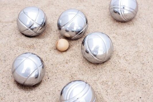 Six metal boules and a small wooden ball on sand.