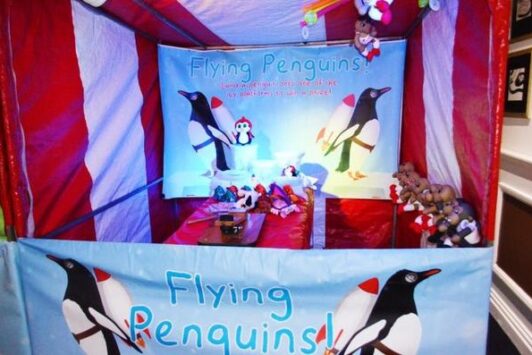 Flying Penguins fair stall with penguin decorations and stuffed animal prizes.