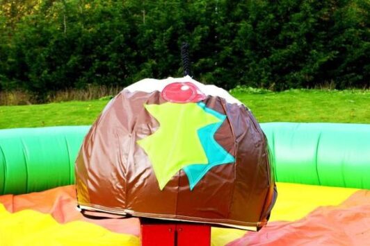 Inflatable Christmas pudding ride in a green and yellow outdoor play area.