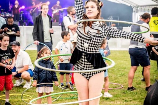 A circus performer spins multiple hula hoops at an outdoor event under a large tent.