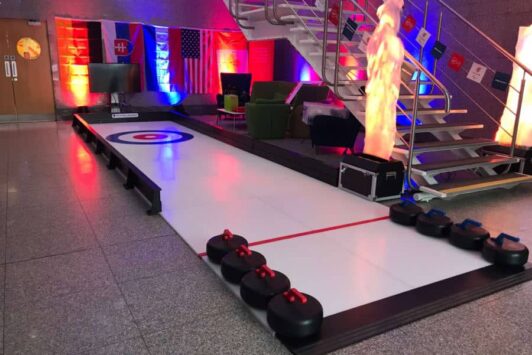Indoor curling lane with curling stones, flags on the wall, and colorful lighting.