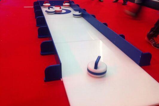 Children’s curling lane with curling stones set up on a white playing surface over a red floor.