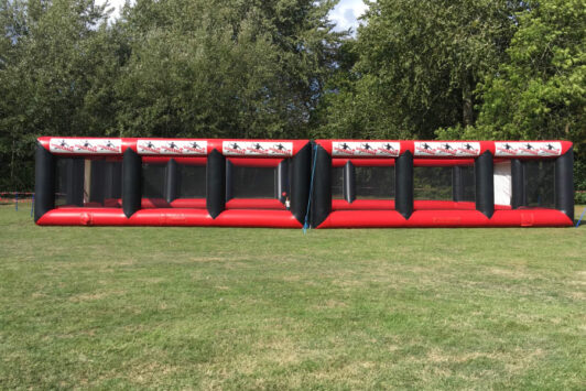 Red and black inflatable dodgeball arena set up on a grassy field with trees in the background.