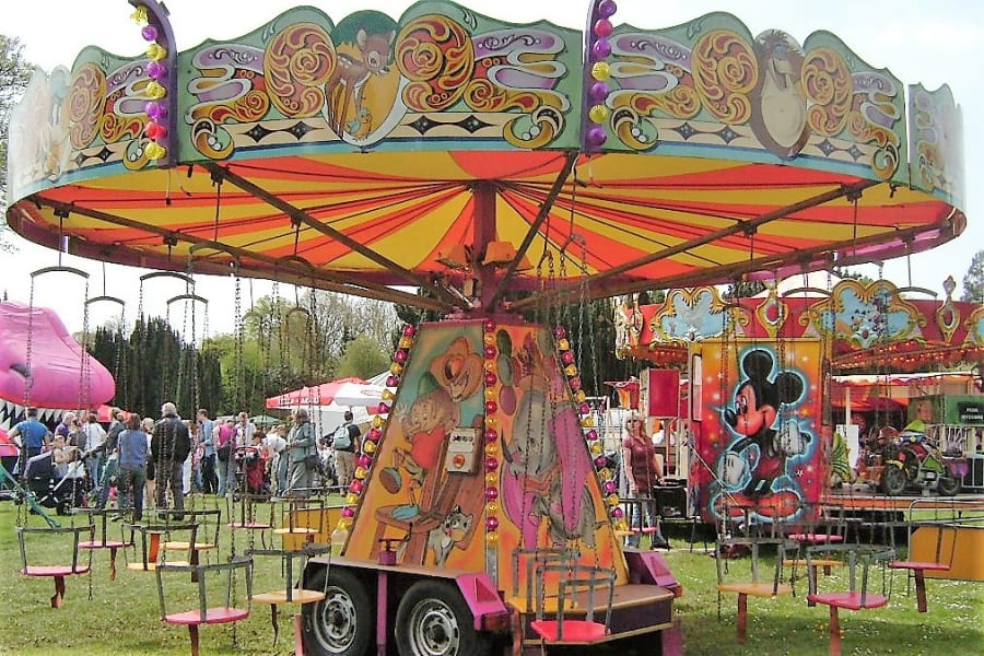 Fun-Fair-Ride-Childrens-Chairoplanes Colorful children's chairoplane ride at a fun fair, with empty swings and people in the background.