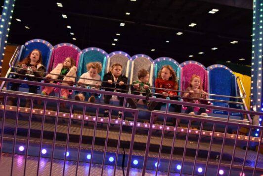 Children sitting on a colorful funfair ride with bright lights and glittery seats.