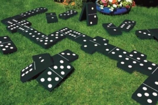 Giant dominoes are scattered on green grass outdoors.