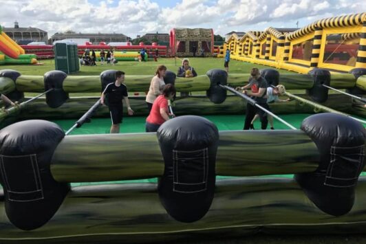 People playing human table football outdoors in an inflatable arena on a sunny day.