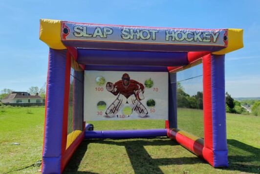 Inflatable slap shot hockey game setup on grass under a clear blue sky.