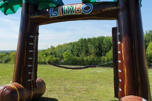 Inflatable limbo game setup on grass with palm tree design, under a clear blue sky.