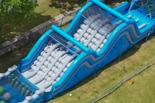 Large blue inflatable obstacle course set up outdoors on grass.