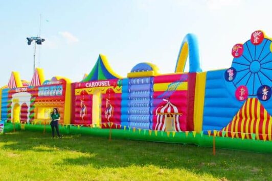 Colorful inflatable obstacle course with fun fair and circus designs set up outdoors on grass.