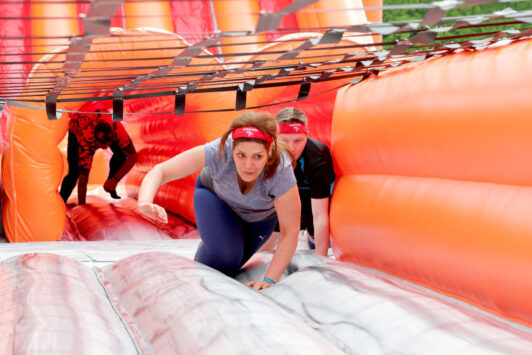 People crawling through an inflatable obstacle course with orange walls and a net overhead.