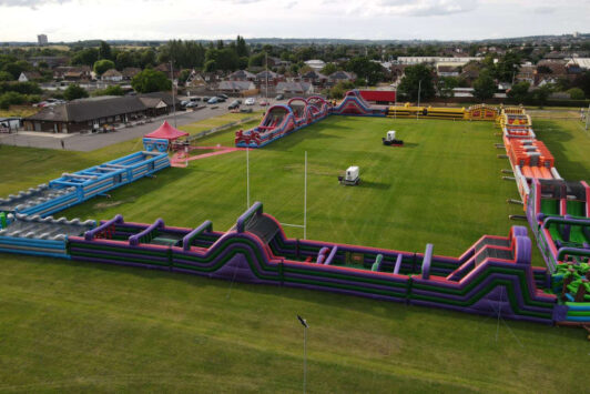 Large inflatable obstacle course set up on a grassy field, viewed from above.