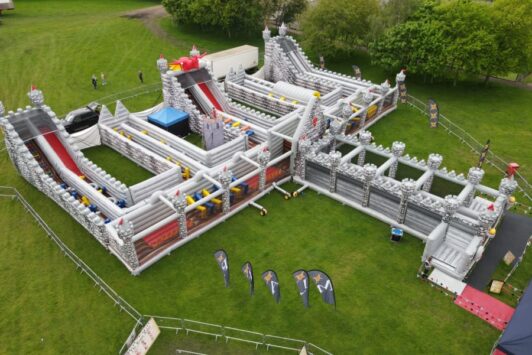 Large inflatable obstacle course with castle design set up on a grassy field.