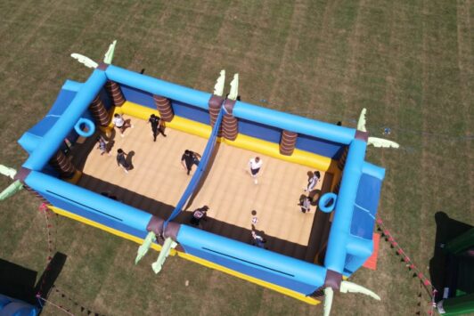 Aerial view of people playing inside an inflatable volleyball court on grass.