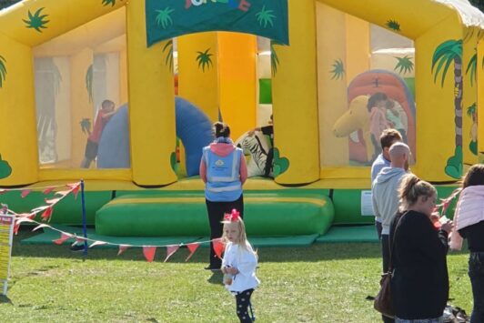 Children and adults near a yellow jungle-themed inflatable bouncer at an outdoor event.
