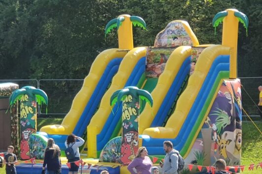 Large inflatable jungle slide with palm tree decorations, surrounded by people at an outdoor event.
