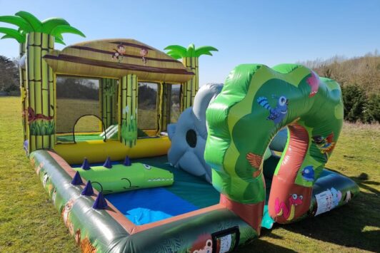 Inflatable jungle-themed play zone with animal and tree designs on a grassy field.