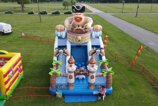 Inflatable pirate-themed slide and castle on a grassy field, with a person sitting in front.