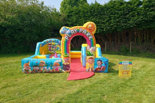 Colorful inflatable play park set up on grass with cartoon characters and a sign nearby.