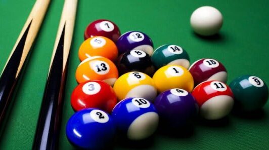 Pool balls racked on a green table, with two pool cues and the cue ball nearby.